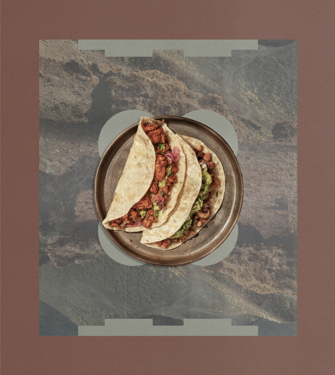 Two tacos on a plate over a rocky landscape collage in a terracotta frame